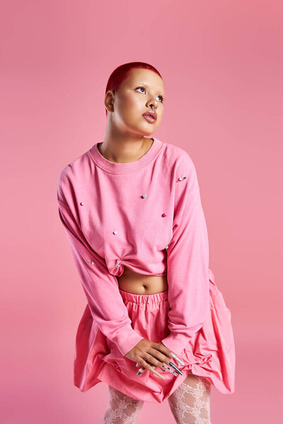 A bold young woman with short pink hair showcases her creative style against a pink background.