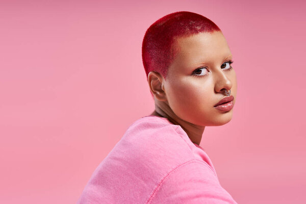 This young woman with short pink hair and a nose piercing displays her unique fashion sense in a vibrant studio.