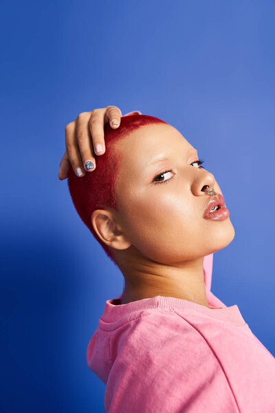 A confident young woman with striking pink hair showcases her unique style against a bright blue backdrop.