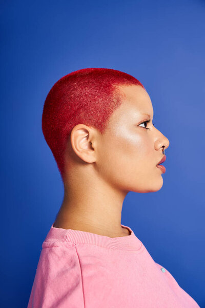 Молодая женщина уверенно демонстрирует свой уникальный стиль с короткими розовыми волосами и дерзким пирсингом носа в студии.