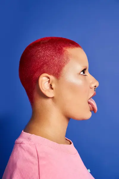 stock image A young woman showcases her vibrant pink hair and playful attitude against a bright blue background.