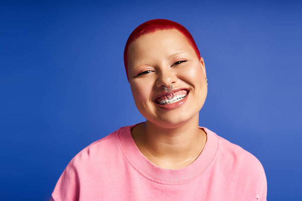 In a lively studio, a young woman with short pink hair confidently displays her bold fashion sense.