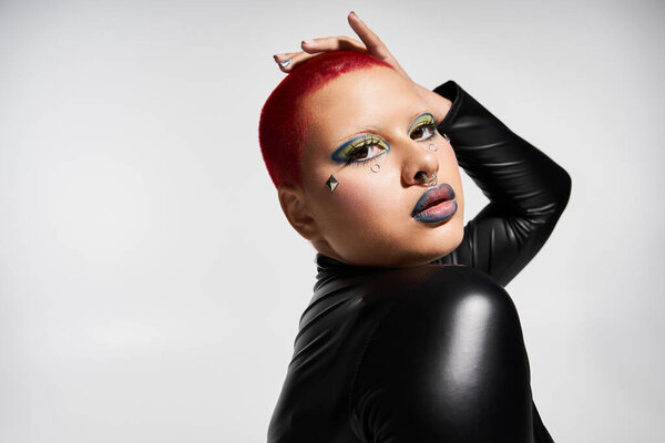 Смелая молодая женщина с короткими розовыми волосами уверенно демонстрирует свою отличительную моду в художественной студии.