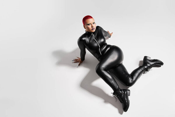 Уверенная молодая женщина в элегантном наряде творчески позирует в яркой, минималистской студийной обстановке.