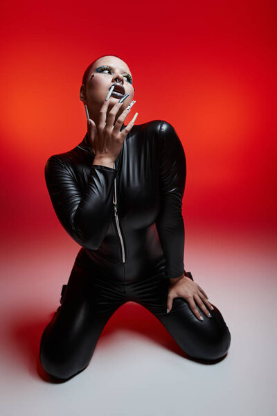 A confident young woman in a striking outfit showcases her short pink hair and nose piercing in bold light.