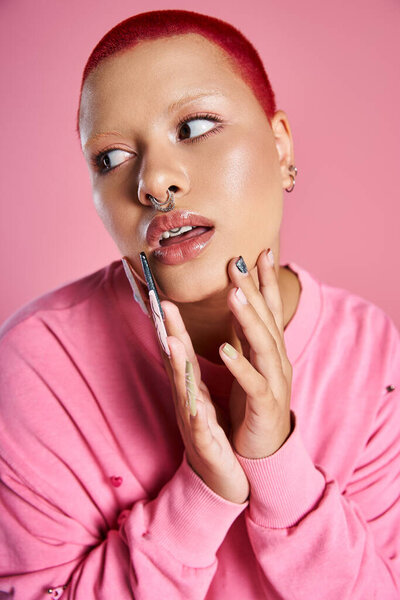 A confident young woman with striking pink hair showcases her unique fashion sense against a colorful background.