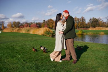 A cozy couple embraces warmly amidst autumn colors, enjoying a peaceful lakeside moment. clipart