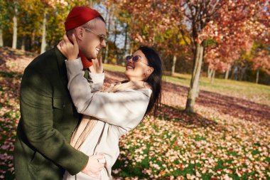 A warm and loving couple enjoys a joyful moment surrounded by vibrant autumn foliage. clipart