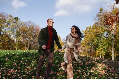 Two loving individuals enjoy a walk amidst falling leaves, clad in cozy autumn attire. clipart