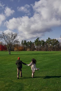 A loving couple embraces the autumn chill, laughing as they sprint across a lush green field. clipart