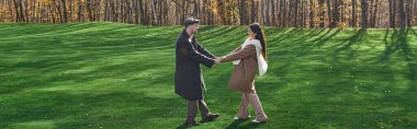 A couple in warm, stylish autumn outfits holds hands amidst a vibrant, leaf strewn landscape. clipart