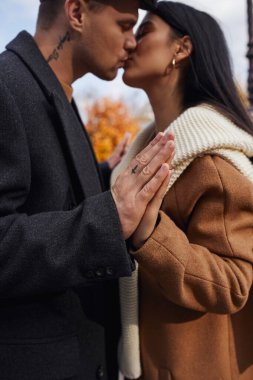 A couple embraces warmly in autumn attire, sharing a tender kiss surrounded by vibrant foliage. clipart