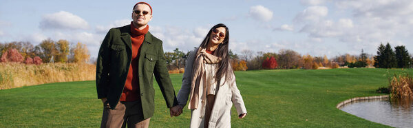 A couple strolls hand in hand through a picturesque park on a warm autumn day.
