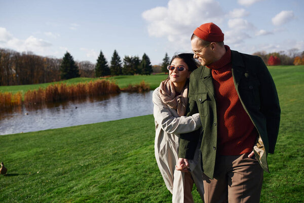 A couple enjoys a serene walk by a tranquil lake, wrapped in cozy autumn attire.