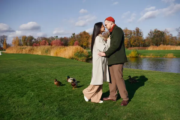 stock image A cozy couple embraces warmly amidst autumn colors, enjoying a peaceful lakeside moment.