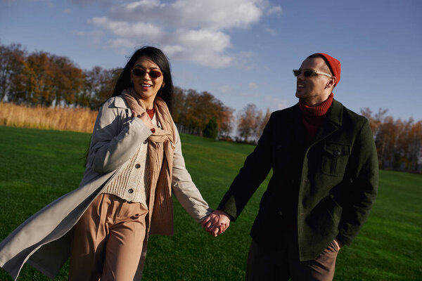 Пара идет рука об руку, одетая тепло в течение осеннего дня, окруженная красочными деревьями.