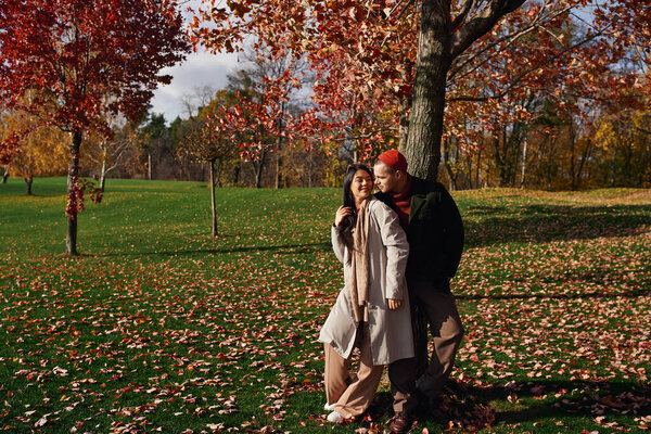 A couple enjoys an affectionate moment outdoors, surrounded by colorful autumn leaves.