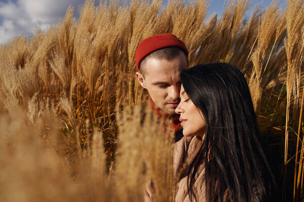 A cozy couple shares an intimate moment surrounded by autumns golden grasses, radiating warmth.