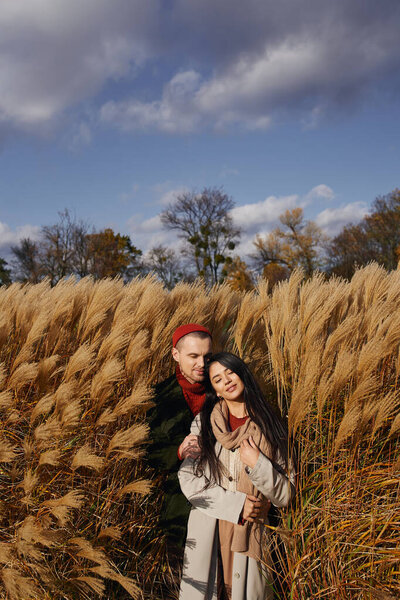 A joyful couple embraces warmly, surrounded by swaying golden grasses on a sunny autumn day.