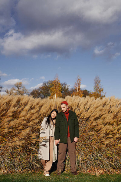 A couple enjoys the beauty of autumn, embracing warmly among golden grasses under a blue sky.