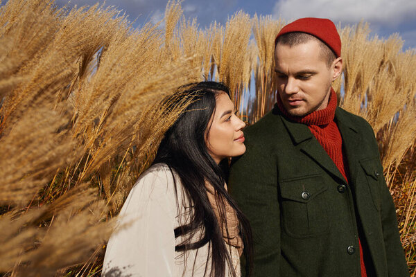 A loving couple embraces each other warmly, surrounded by golden autumn foliage under a bright sky.