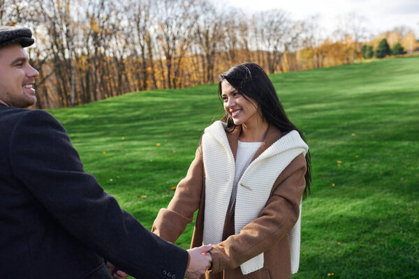 A loving couple shares laughter while holding hands in a beautiful autumn landscape.