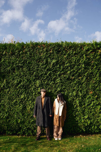 A loving couple stands together, enjoying the warm autumn weather with nature all around them.