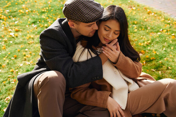 A couple shares an affectionate moment surrounded by vibrant autumn leaves while dressed warmly.