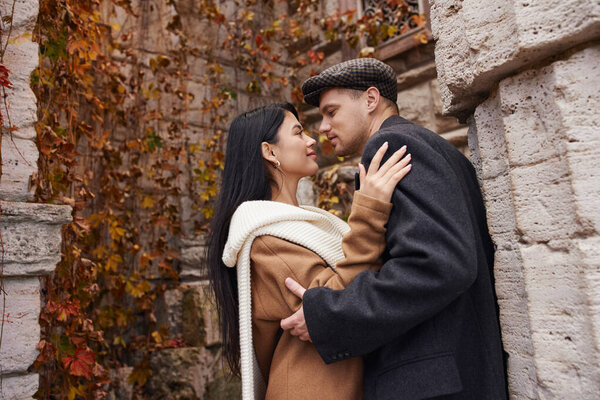 A couple enjoys a tender moment in warm autumn clothing amidst colorful fall foliage.