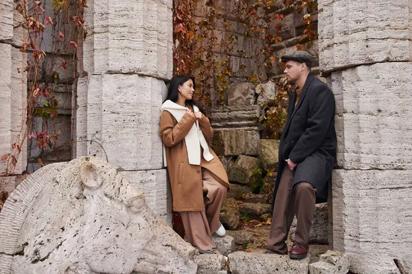 stock image A couple in autumn attire shares a tender moment in a serene, historic spot with foliage.