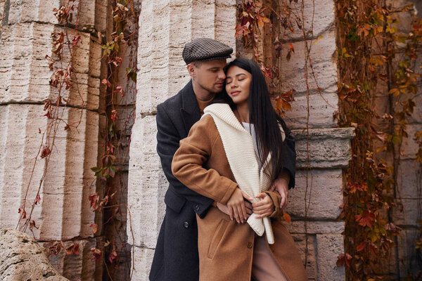 A couple in warm clothes shares a cozy moment in autumn leaves.