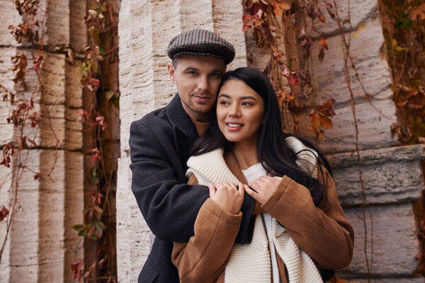 A couple warmly embraces each other, enjoying a serene autumn day amidst colorful leaves.
