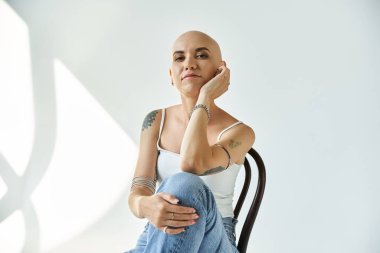 Alopecia hastası genç bir kadın düşünceli bir şekilde bir sandalyeye oturur, özgüvenini ve zarafetini gösterir..
