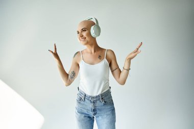 Genç kel bir kadın, kulaklık takarak gülümsüyor. Parlak bir mekanda mutluluğu ifade ediyor..