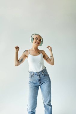 Alopecia hastası genç bir kadın mutlu bir şekilde müziğin tadını çıkarıyor, dingin bir mekanda neşeyle dans ediyor..