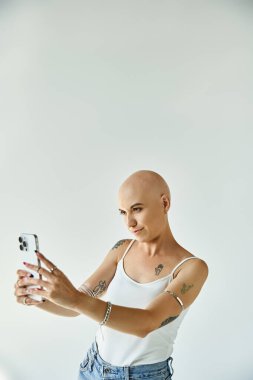 Alopesia hastası genç bir kadın basit beyaz bir arkaplanda neşeyle selfie çekiyor..