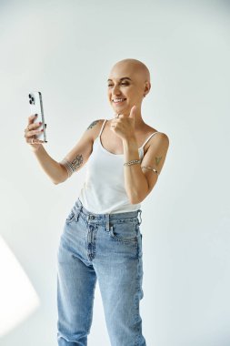Alopecia 'lı genç bir kadın gülümser ve selfie çekerken başparmağını kaldırır..