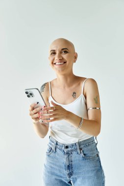 Kel bir kadın, akıllı telefonuyla iyi aydınlatılmış bir alanda iletişim kurarken neşe saçıyor..