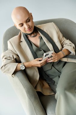 Kendine güveni olan genç bir kadın şık bir sandalyede rahatlar, akıllı telefonuyla meşgul olur..