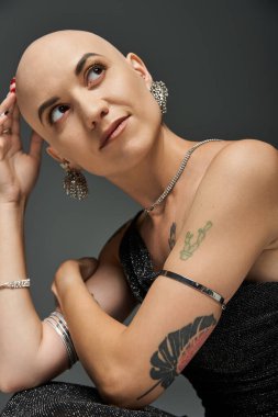 Kel ve saçları dökülmüş genç bir kadın zarifçe poz verir, özgüven ve güç yayar..