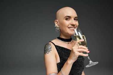 Genç kel bir kadın şık bir ortamda elinde bir kadeh şampanya tutarken sıcak bir şekilde gülümsüyor..