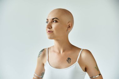 A young woman with alopecia stands confidently, displaying her tattoos and inner strength. clipart