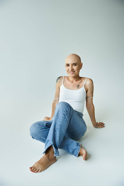 Молодая лысая женщина с алопецией сидит небрежно на гладкой поверхности, источая уверенность и изящество.