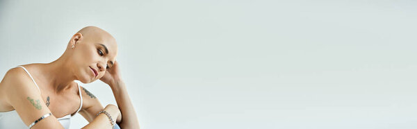 Молодая лысая женщина вдумчиво смотрит вниз, демонстрируя свою уникальную красоту.