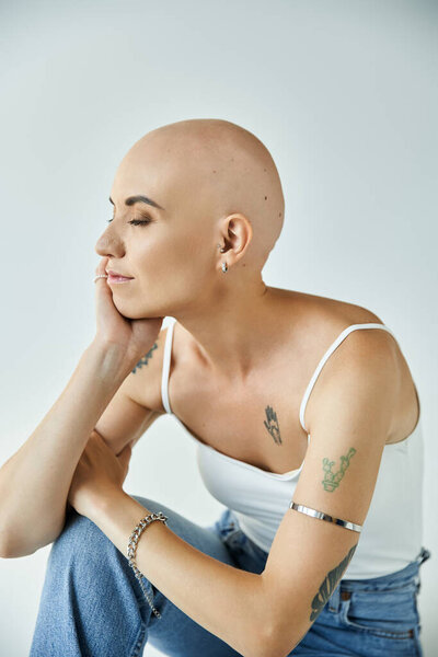 Молодая лысая женщина с алопецией выражает спокойствие, сидя в яркой студии.