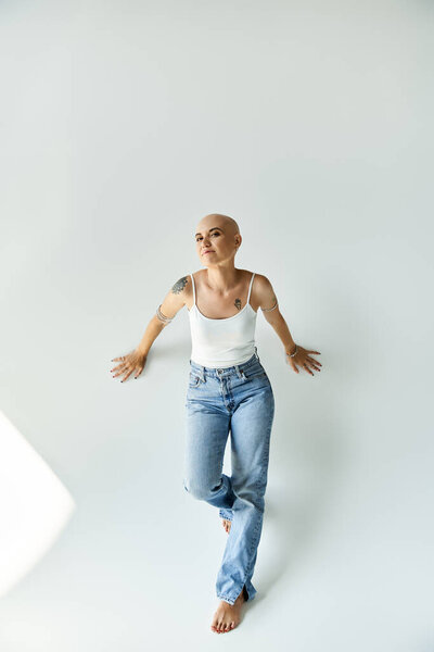 A young bald woman embraces her unique beauty while striking a pose against a soft backdrop.