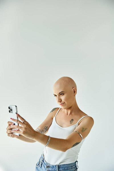 Молодая женщина с алопецией с радостью снимает селфи на простом белом фоне.