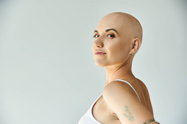 Молодая лысая женщина демонстрирует свою природную красоту с уверенным выражением лица и нежной позой.