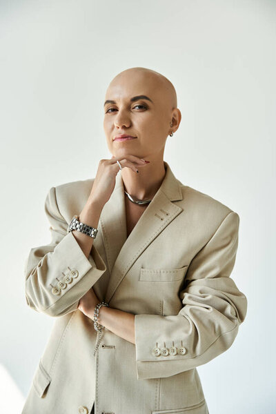 Уверенная в себе молодая женщина с алопецией сияет в стильном бежевом одеянии, демонстрируя свою красоту.