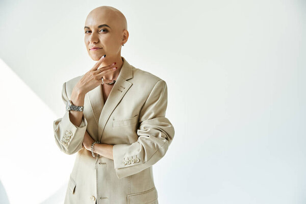 A young bald woman confidently poses in a stylish beige suit, radiating empowerment.